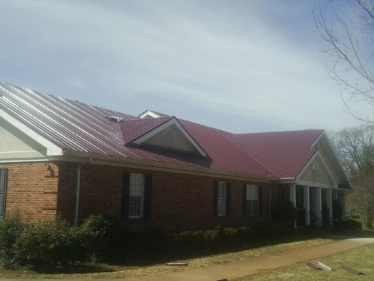 Red metal roof with gabled entries on a long brick building, from a Hail Damage Roof Repair job in Broomall