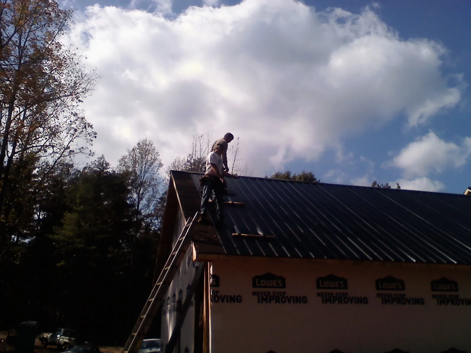 Roofer fastening dark metal panels high against a cloudy sky, from a Roof Inspection job in Broomall
