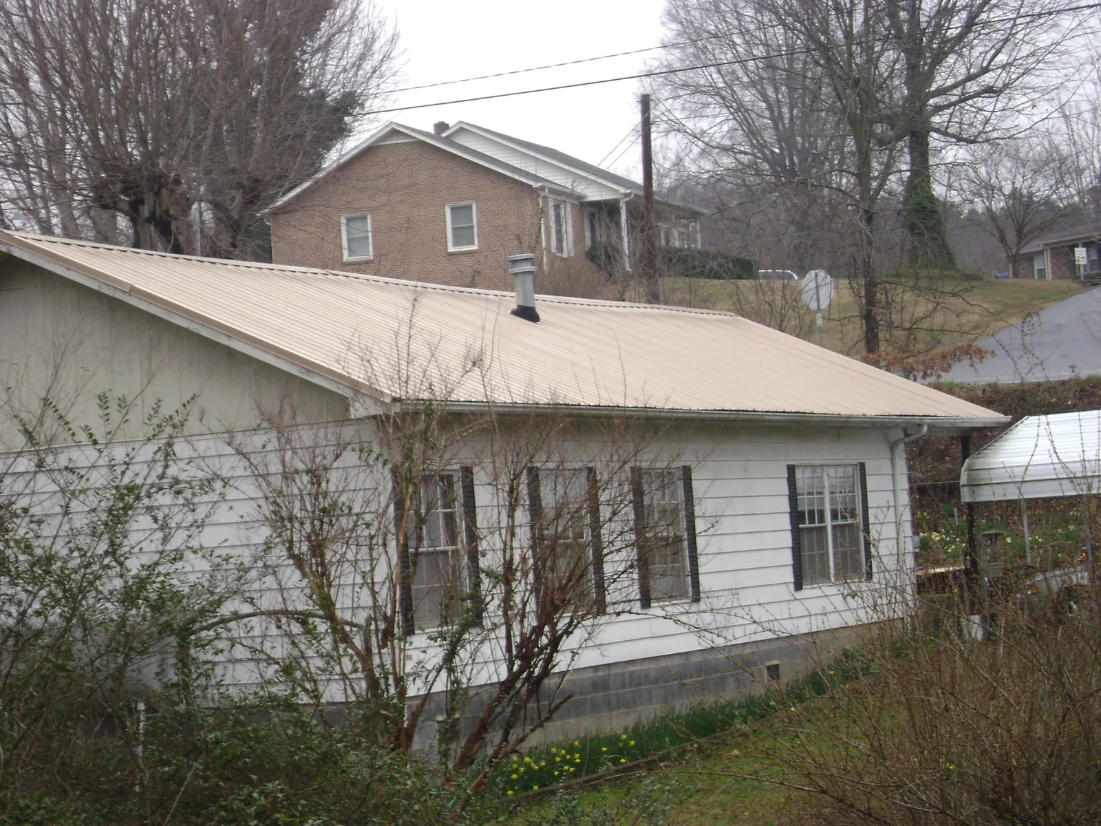 Tan metal roof on a white sided house set into a hillside in Broomall